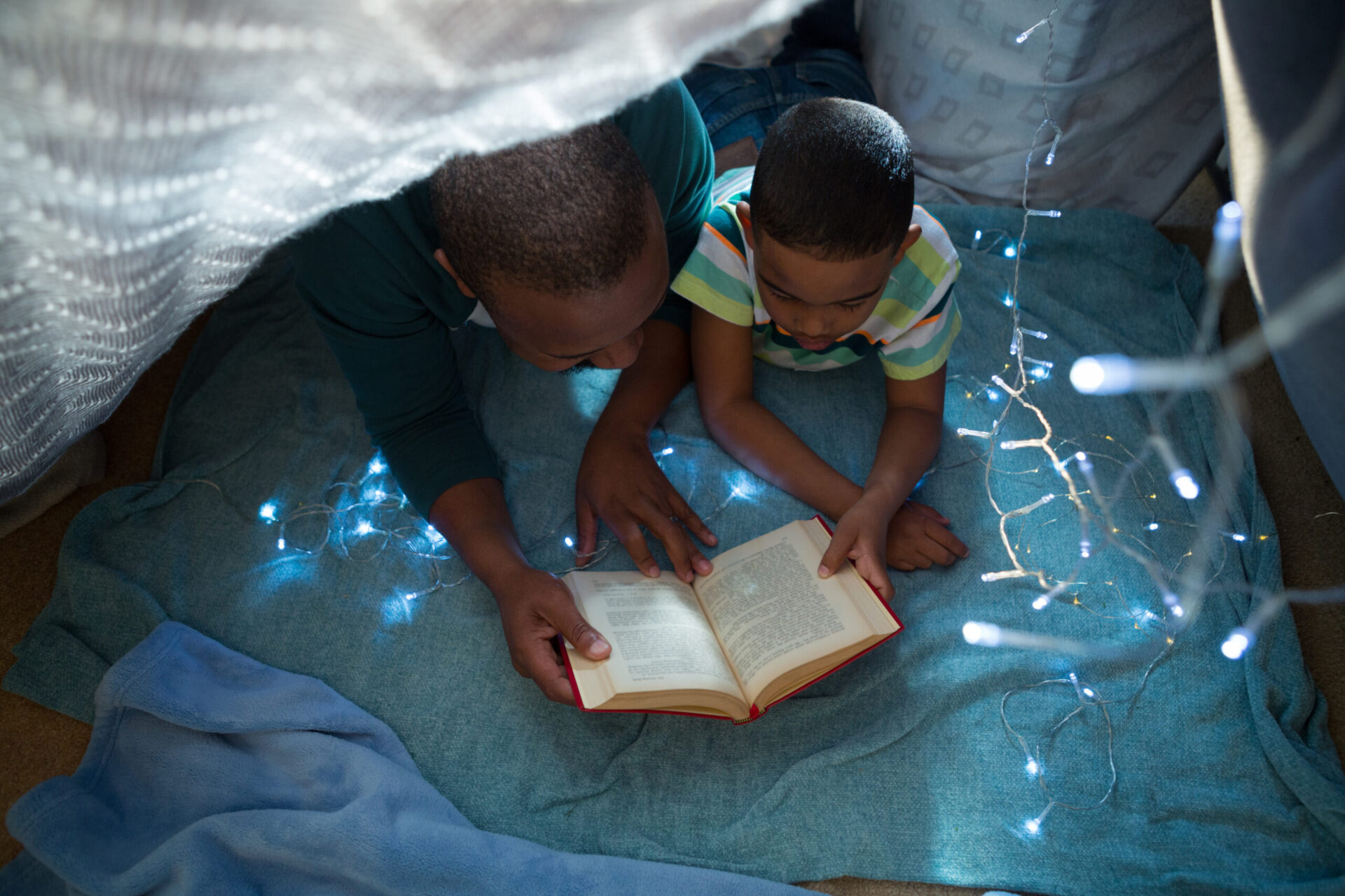 Father And Son Reading Book In Bedroom At Home