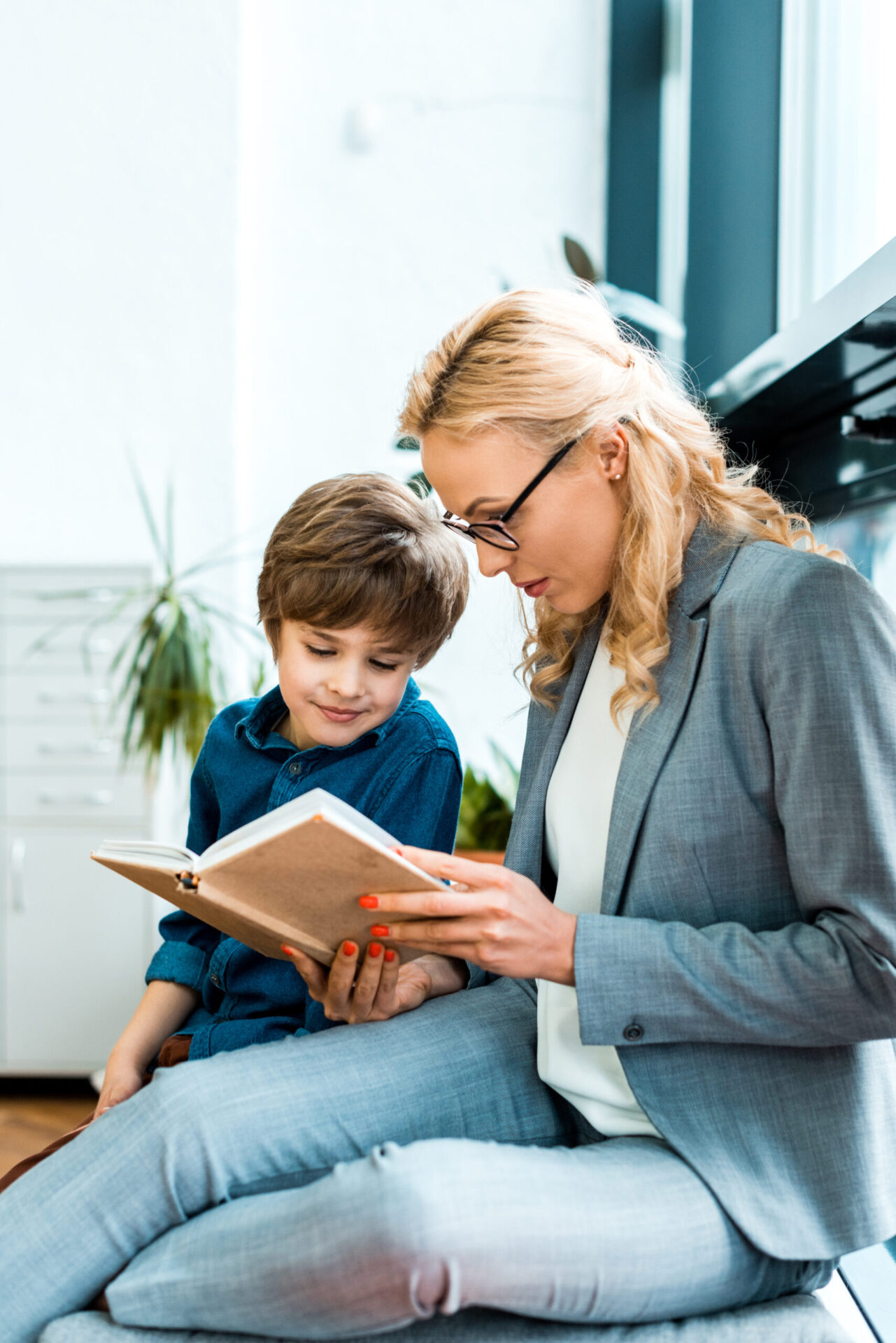 Attractive Woman In Glasses Sitting On Floor And Reading Book With Cute Kid